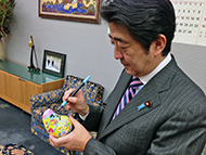 Prime Minister Shinzo Abe decorates his tumble doll.